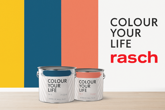 alt="Rasch Colour your life – kreative Tapetenkollektion mit Farbakzenten in Gelb, Blau und Koralle. Zwei Farbdosen auf hellem Holzboden vor modernem Hintergrund."